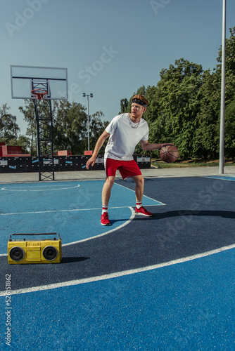 young sportsman playing basketball near tape recorder on modern court