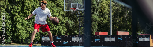 full length of young sportive man playing basketball on court, banner