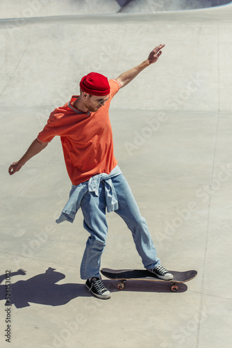 full length of stylish man with outstretched hands skateboarding in skate park