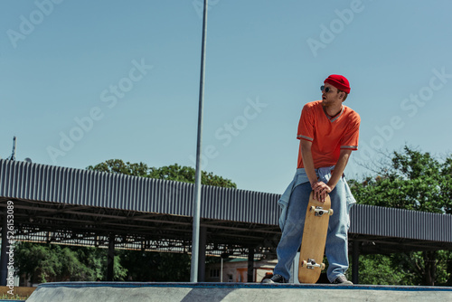 full length of fashionable man with skateboard looking away outdoors