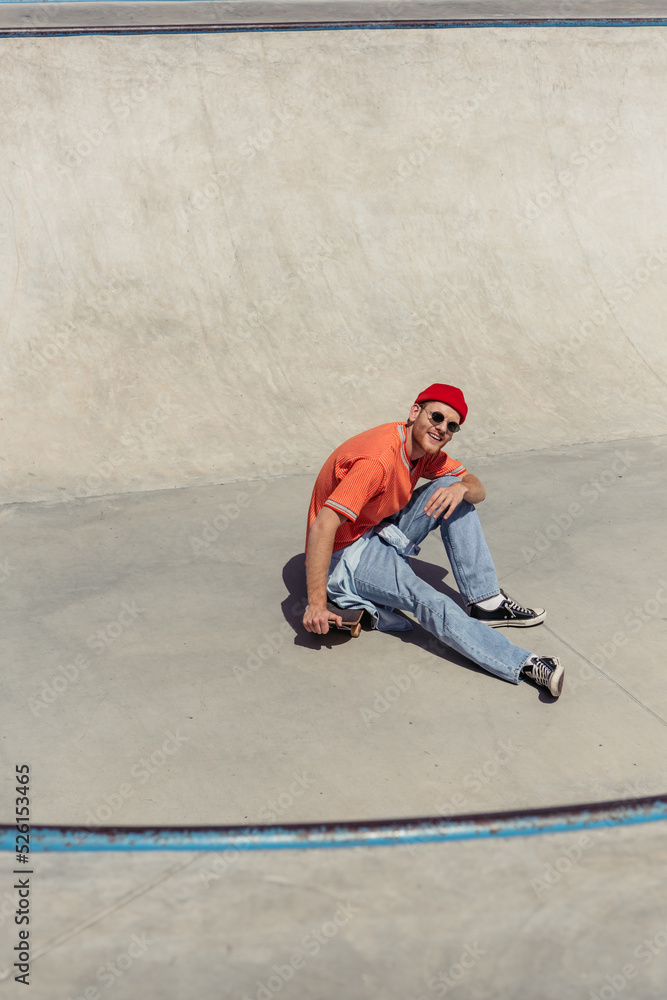 high angle view of smiling man in trendy clothes sitting on skate and looking at camera high angle view of smiling man in trendy clothes sitting on skate and looking at camera