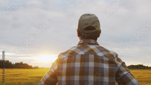 Farmer in front of a sunset agricultural landscape. Man in a countryside field. Country life, food production, farming and country lifestyle. © Acronym
