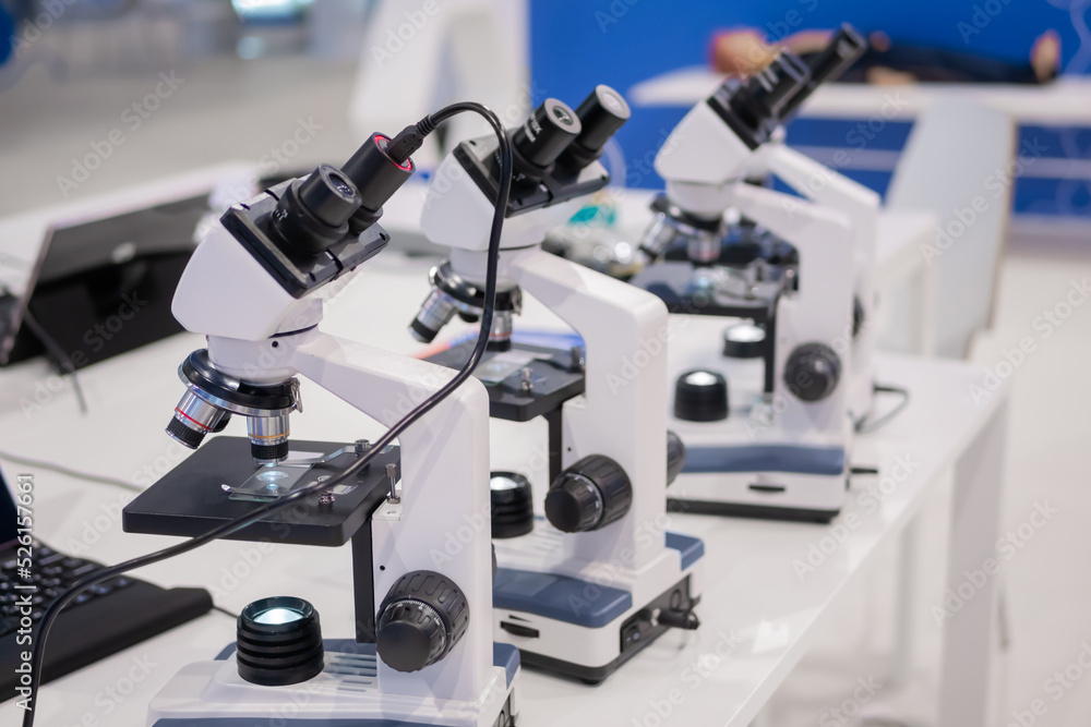 Microscopes on white table at medical technology exhibition, trade show. Laboratory equipment, science, medical, optical, pharmaceutical and education concept Microscopes on white table at medical technology exhibition, trade show. Laboratory equipment, science, medical, optical, pharmaceutical and education concept