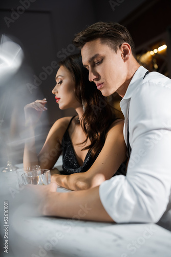 Man in shirt holding glass near elegant girlfriend in bar