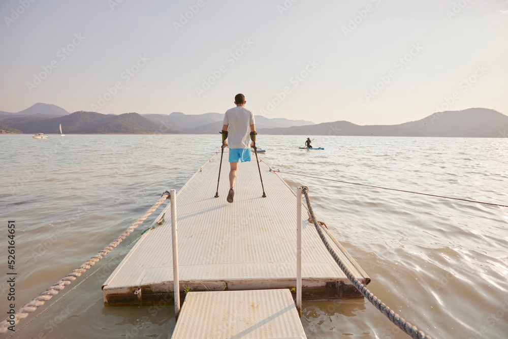 Naklejka premium Back view of disabled man walking on pier in lake