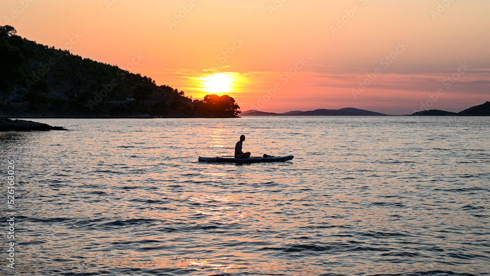 Silhouette of woman sitting on stand up paddle board on the sea. Woman enjoying on Paddle-board at summer. SUP