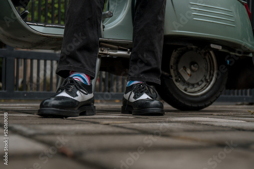 These hand-made black-and-white wingtip shoes with loafers sole made from genuine leather are being worn to hang out with an old green Vespa