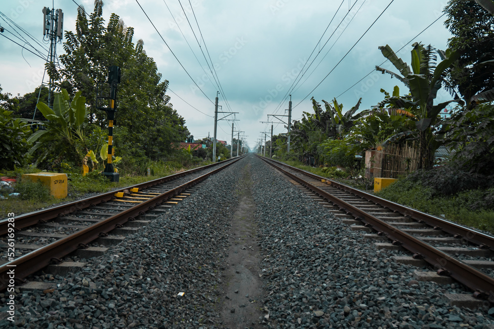 Details of the railroad track made of iron, wood and gravel in a suburban area on a cloudy day in Indonesia