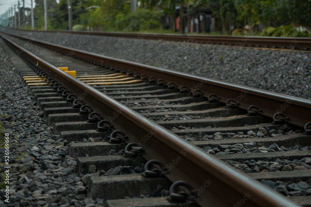 Naklejka premium Details of the railroad track made of iron, wood and gravel in a suburban area on a cloudy day in Indonesia