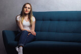 Attractive young adult housewife woman sitting on the couch and looking at the camera in her house