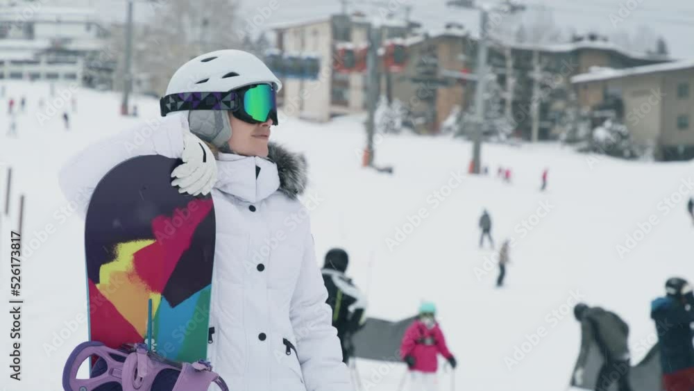 Snowboarder on background of ski slope at Snowmass ski resort. Slow motion close up portrait of athletic female tourist on snowy winter day with snowboarders shredding the slopes on blurred background Snowboarder on background of ski slope at Snowmass ski resort. Slow motion close up portrait of athletic female tourist on snowy winter day with snowboarders shredding the slopes on blurred background