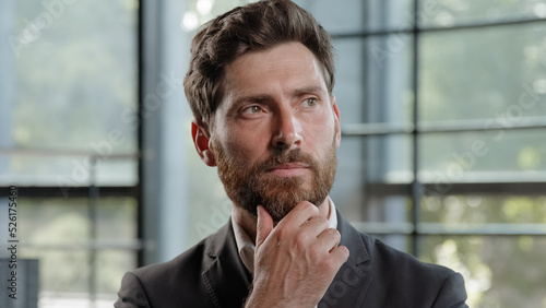 Pensive adult Caucasian bearded man 40s businessman posing looks around thinks pondering pensive thoughtful thinking about job project problem solutions comes up with ideas raised finger up in office