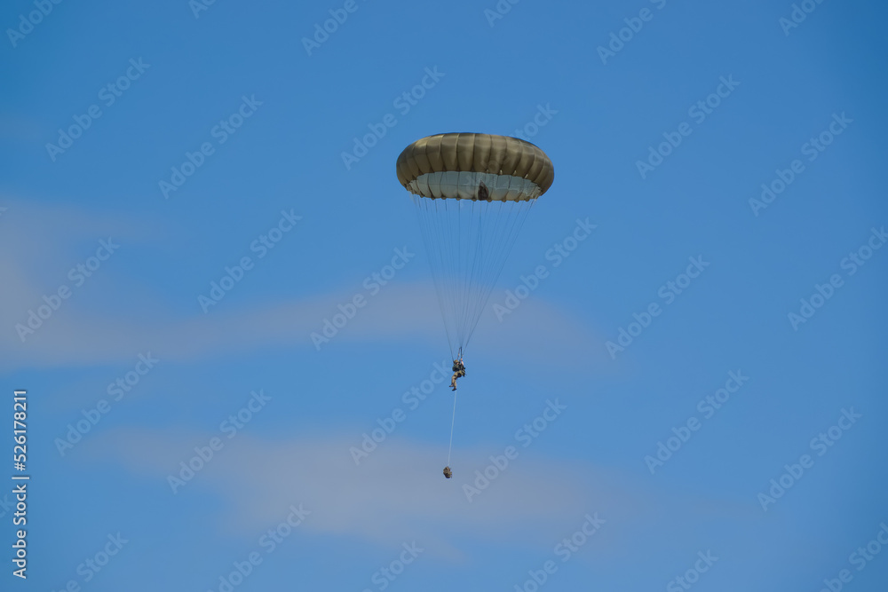 British army paratrooper parachuting on an overhead assault , wearing body armour and webbing with weapons and daysacks suspended by rope below, blue sky British army paratrooper parachuting on an overhead assault , wearing body armour and webbing with weapons and daysacks suspended by rope below, blue sky