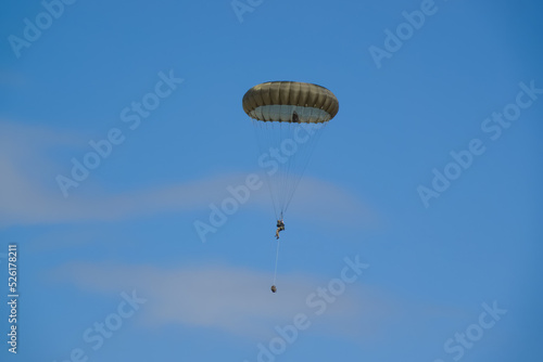 British army paratrooper parachuting on an overhead assault , wearing body armour and webbing with weapons and daysacks suspended by rope below, blue sky