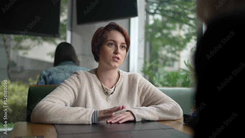 Young woman in conversation with friend at coffee shop. Red hair girl talking sharing information sitting at restaurant Young woman in conversation with friend at coffee shop. Red hair girl talking sharing information sitting at restaurant