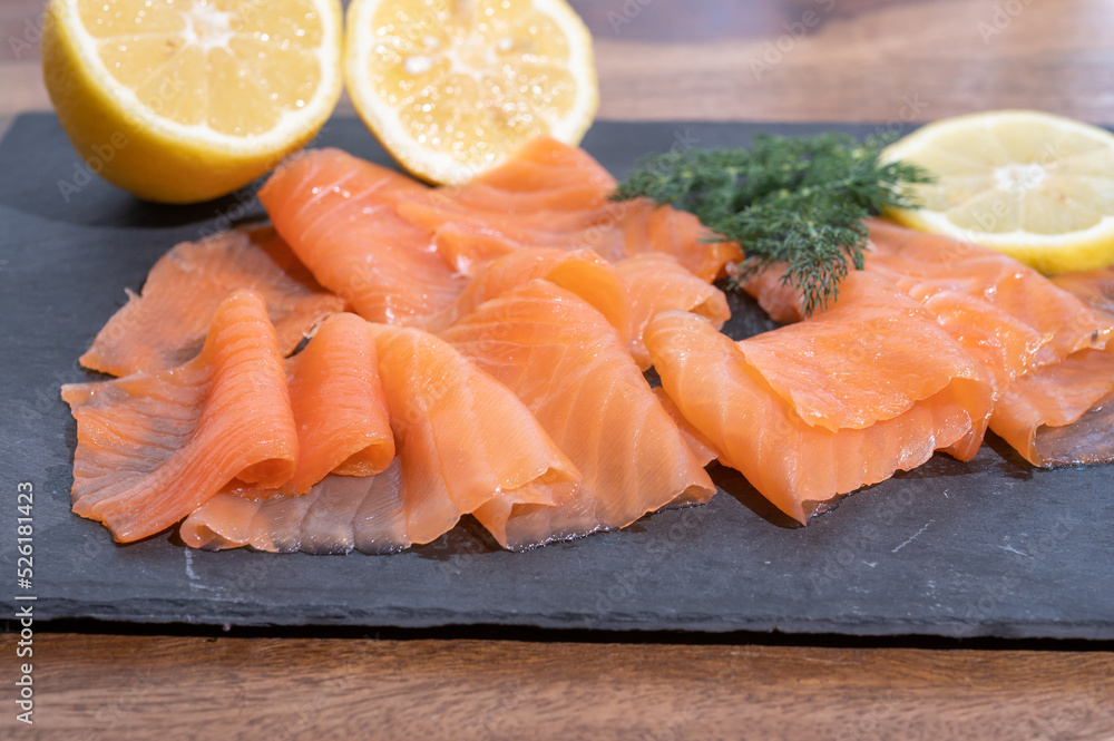 Slices of tasty smoked Scottish salmon fish served on black plate with lemon and fresh dill
