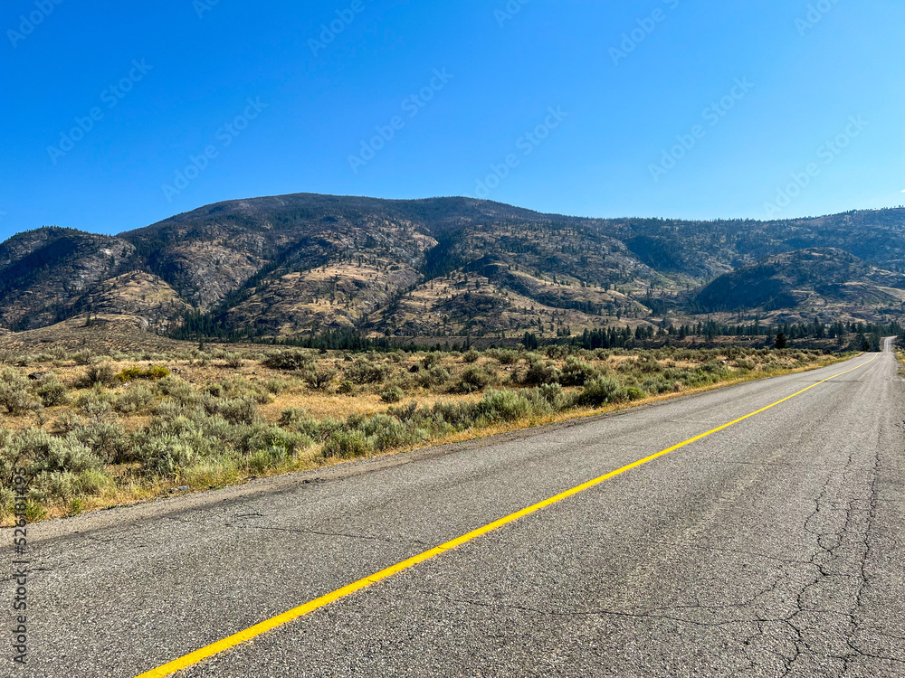Road passing though the desert, mountain view and blue Summer's sky, Okanagan Valley, British-Columbia, Canada