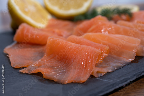 Slices of tasty smoked Scottish salmon fish served on black plate with lemon and fresh dill