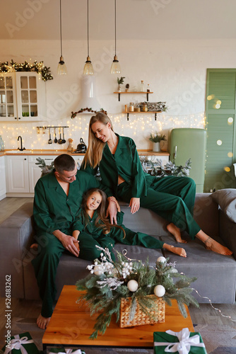New Year, family mom, dad and little beautiful daughter in the kitchen in bright colors, decorated for the holiday, in the same emerald linen pajamas