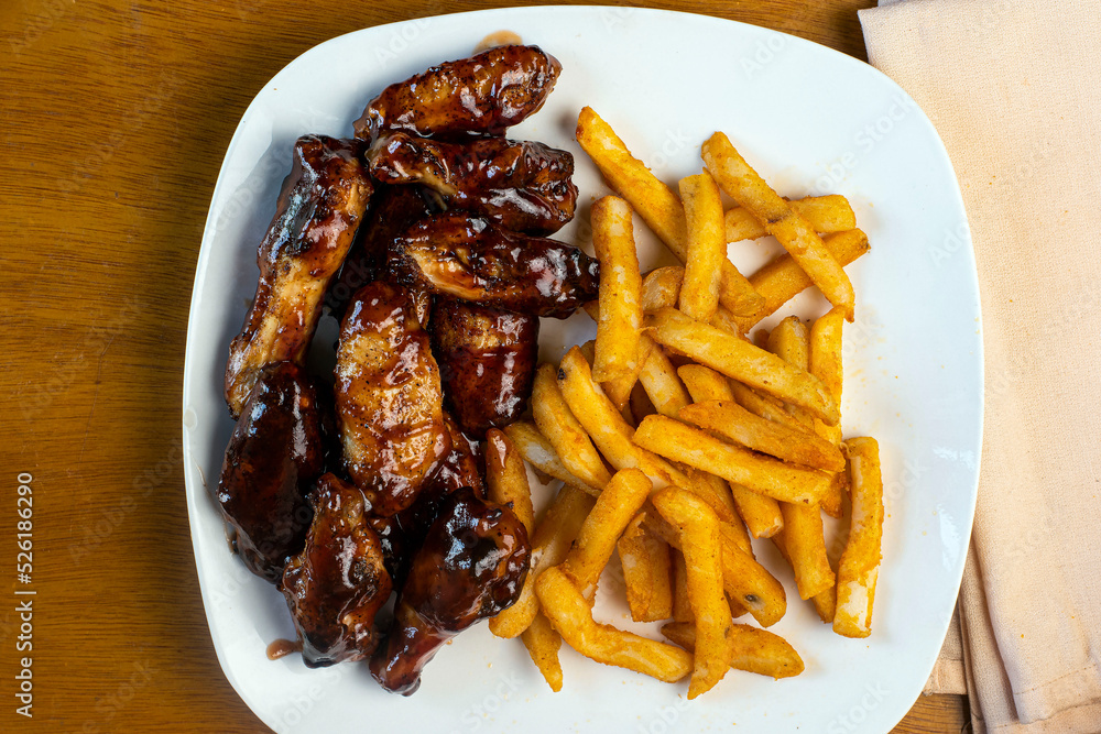 chicken wings covered in barbecue sauce with a side of fries Stock