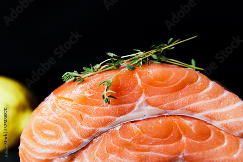 Fresh raw salmon fillet with seasonings and herbs, close-up on black background.