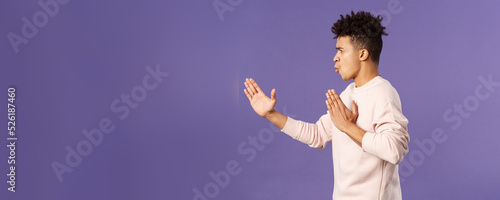 Profile portrait of young hispanic guy with dreads acting like he is ninja or martial arts fighter, practice his kung-fu or taekwondo skills, standing purple background photo