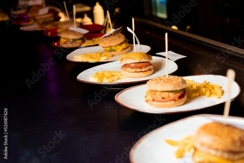 A lot of burgers on white plates lie in a row on a black table