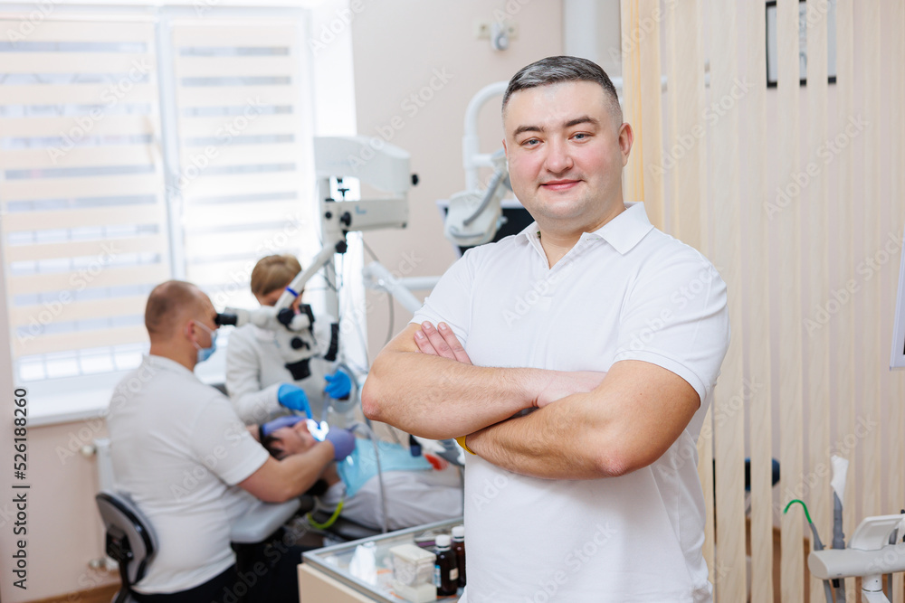 Obraz premium The dentist is in his dental office. A dentist in a white uniform treats a patient's teeth with a dental microscope. Dental office