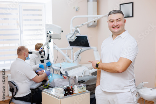 The dentist is in his dental office. A dentist in a white uniform treats a patient's teeth with a dental microscope. Dental office