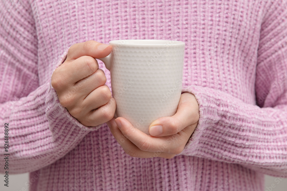 Tea in a white mug in the hands. A girl in a pink sweater holds a white porcelain mug. layout. Close-up. Tea in a white mug in the hands. A girl in a pink sweater holds a white porcelain mug. layout. Close-up.