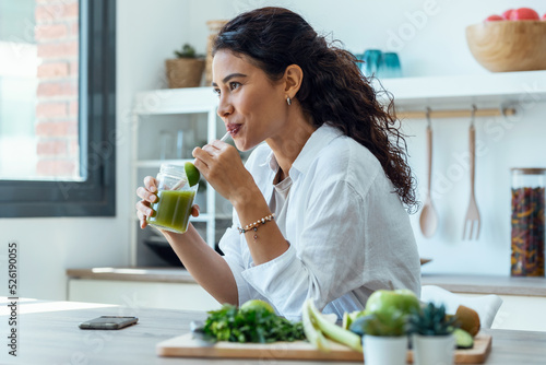 Pretty woman looking to sideways while drinking fruit detox juice in the kitchen at home. photo