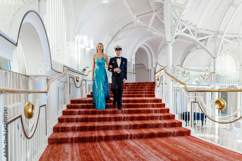 Foto Ein deutscher Marinesoldat schreitet mit seiner Begleiterin in hellblauem Abendkleid die Stufen im Steigenberger Grand Hotel Petersberg auf einem roten Teppich hinab