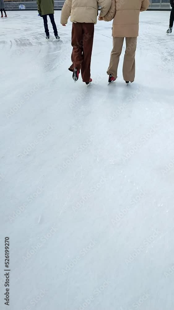 People skating on public open-air ice skating rink in city on winter day. People skating on ice rink. Legs, back, ice rink. Winter holidays, activities ,recreation ,rest, sport. Vertical video People skating on public open-air ice skating rink in city on winter day. People skating on ice rink. Legs, back, ice rink. Winter holidays, activities ,recreation ,rest, sport. Vertical video