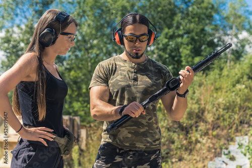 Shooting with a gun or a rifle as a sport and hobby. Caucasian male instructor in moro t-shirt helping out long-haired caucasian girl at a shooting range. High quality photo