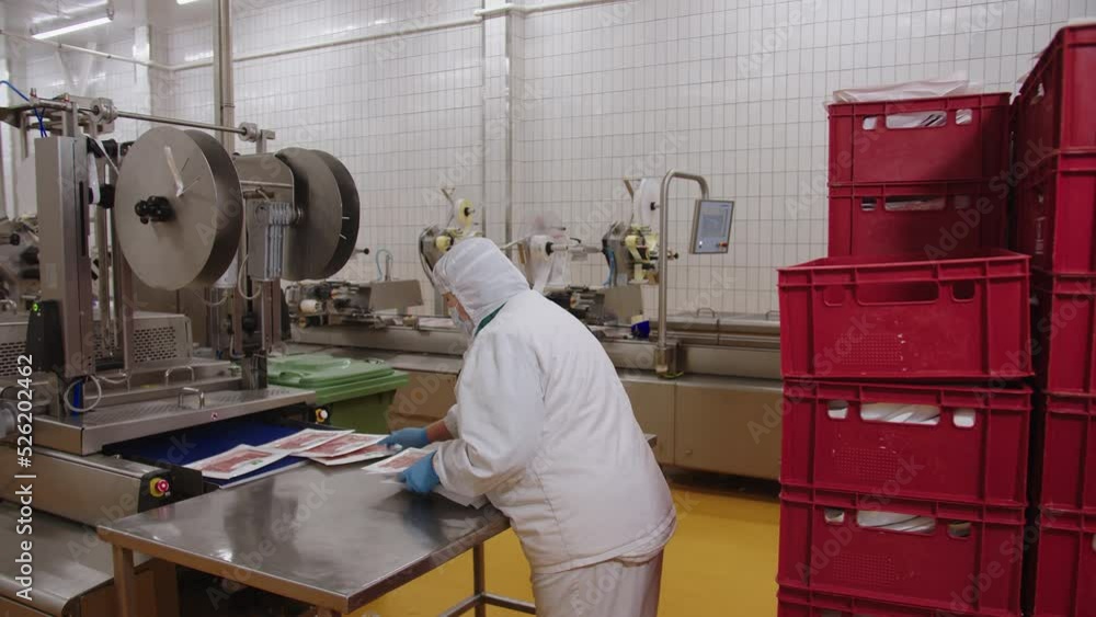 Worker assembles packages of sliced bacon at production line Worker assembles packages of sliced bacon at production line