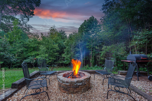 Stone firepit with a glowing fire at dusk surrounded by trees
