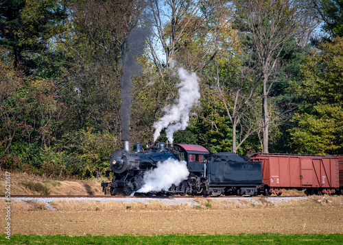 A View of a Restored Steam Freight Train Blowing Smoke and Steam Traveling Along a Rural Countryside on a Sunny Day