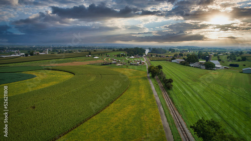 Drone View of Rural Countryside, With Farmlands, barns and Silos. With a Single Railroad Track, on a Blue, Cloud and Sunny Sky.