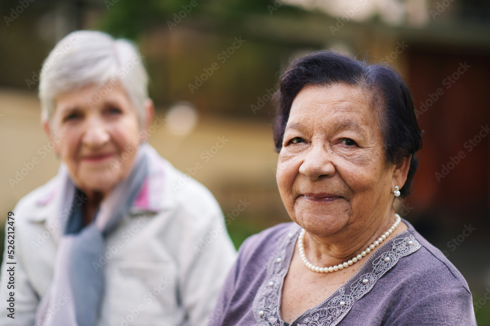Two elderly women sitting on bench in park smiling happy life long friends enjoying retirement Two elderly women sitting on bench in park smiling happy life long friends enjoying retirement