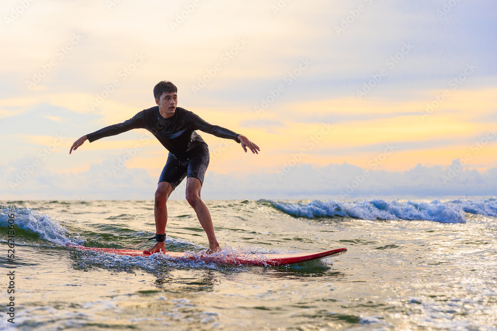 Young teen boy surfer riding waves on soft board in Rayong beach, Thailand. Rookie teenager surfboard student playing on water in excited and funny action.