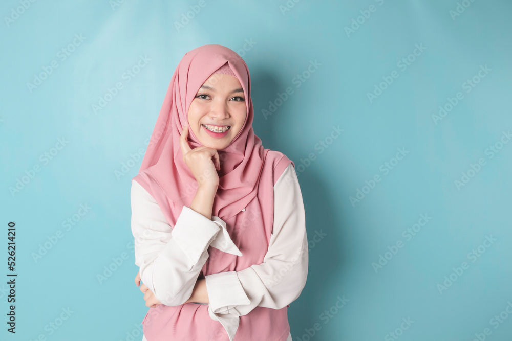 Fototapeta premium Portrait of a cheerful Muslim Asian woman standing and smiling at the camera, isolated on blue background