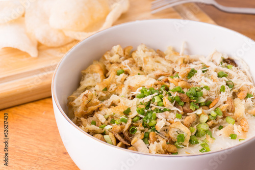 Close up view of Chicken congee or chicken porridge. Equipped with shredded chicken, cakwe or youtiao, garlic crackers, peanuts and spring onions