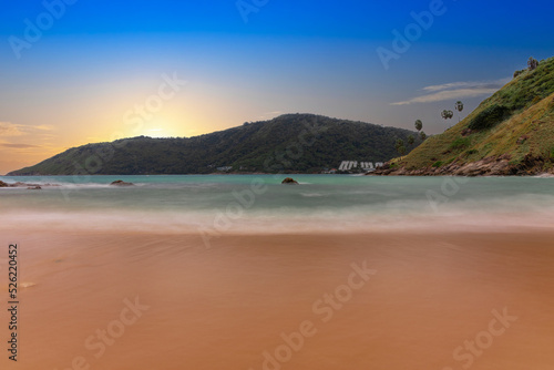 Ya Nui Beach in Phuket Thailand, turquoise blue waters, lush green mountains colourful skies. Phuket is a tropical island many palms