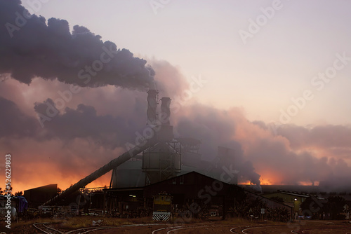 Racecourse sugar mill at sunrise with steam and smoke surrounding it.