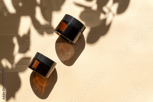 Tela Two jars of amber glass for cosmetics on brown background with floral shadows