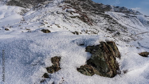 Wallpaper Mural An old weathered boulder is covered with fluffy frost. Lichens are visible on the surface. In the distance is a road running along a snow-covered mountain slope. Blue sky. Altai Torontodigital.ca