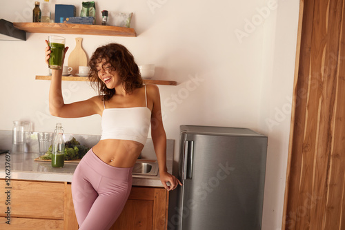 Woman Drinking Green Detox Juice, Smoothie Drink In Kitchen. Happy Smiling Girl With Glass Of Healthy Fresh Raw Vegetable Smoothie At Home. Diet Nutrition Concept 