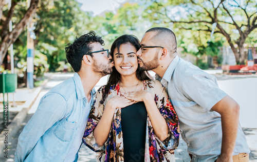 Two men kissing a girl cheek. Portrait of two guys kissing a girl cheek. Two young men kissing a woman cheek outdoor, love triangle concept. Polygamy concept photo