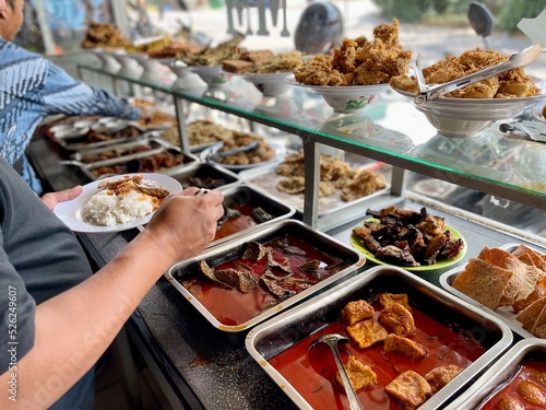 Padang food stalls share a variety of buffet menus with vegetables, chicken curry sauce, beef, eggs, tofu, tempeh. the waiter prepares the food. Menu in glass display case. Asia and asian food. Pile. photo