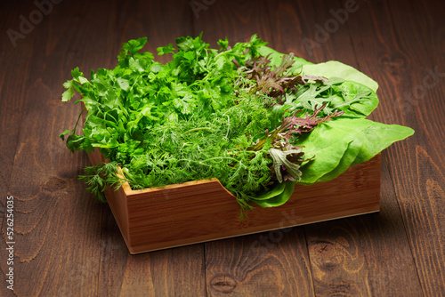 a bunch of green dill, parsley, salad, herbs and other greens in a wooden box, dark wood background, concept of fresh vegetables and healthy food